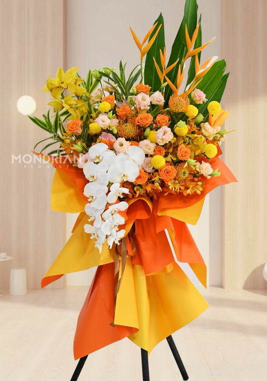 a chic tripod shop opening flower stand with orange and yellow flowers including orchids, roses and bird of paradise