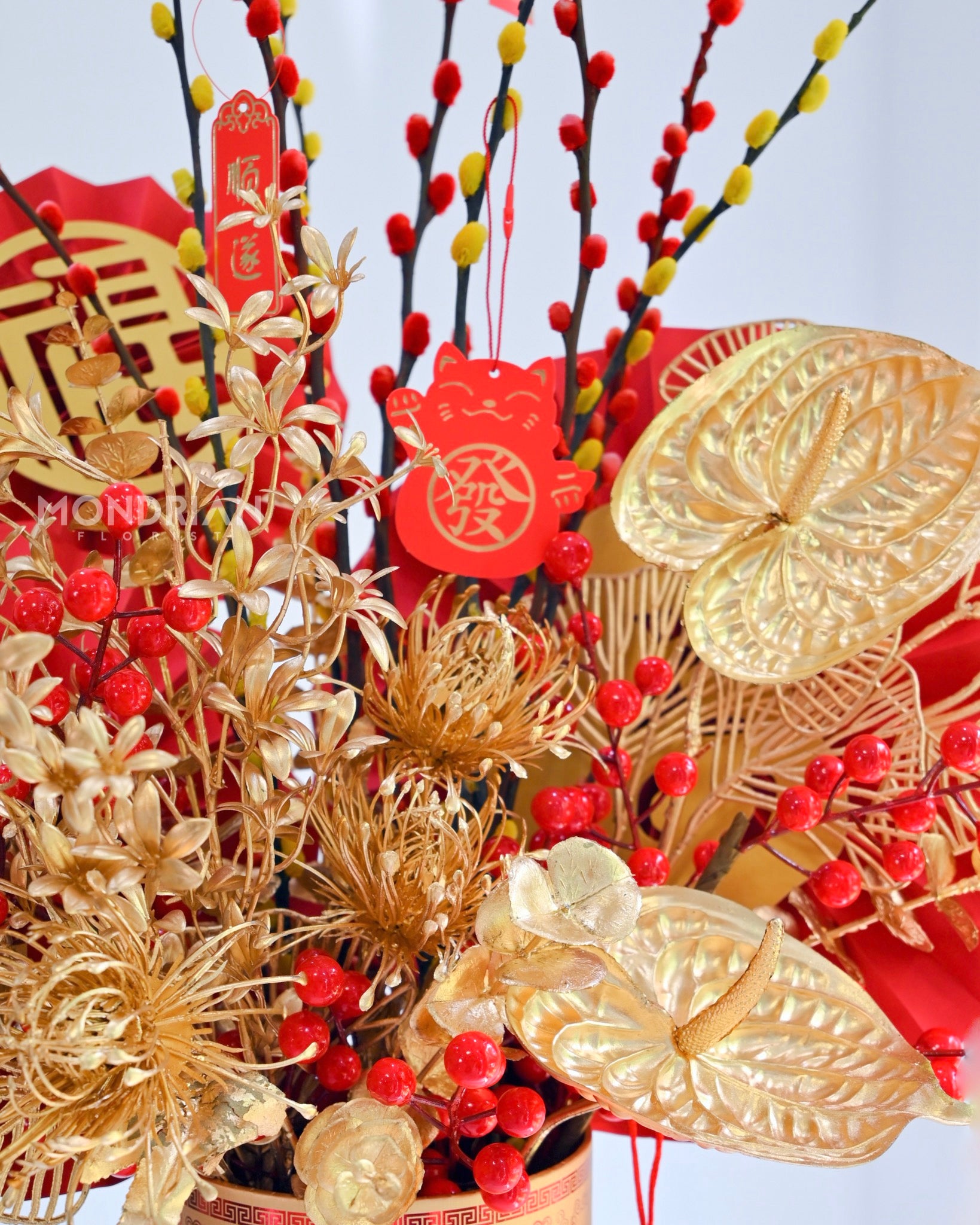 close up of a chinese new year arrangement with red and orange willow buds and golden artificial flowers
